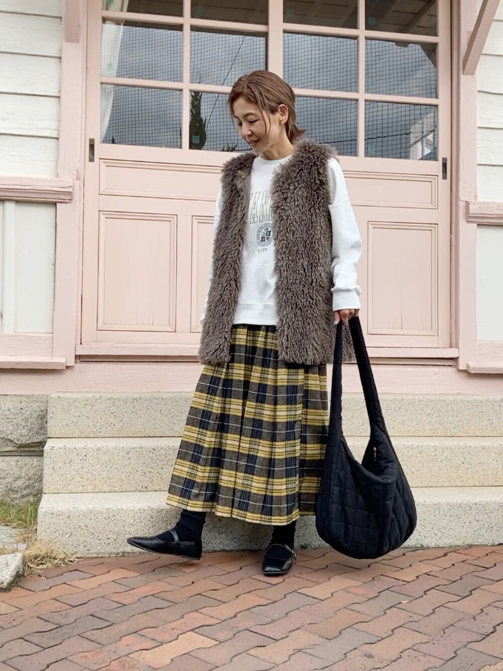 ホワイト系のスウェット、グレー系のベスト、イエロー系のスカートを着用したレディースの秋コーディネートの1枚目の写真