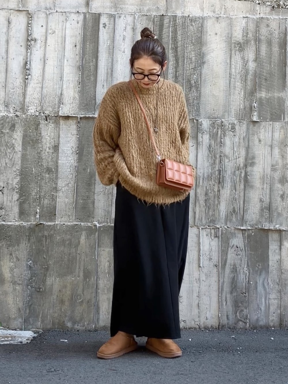 ブラック系のジャンパースカート、ブラウン系のニット/セーター、ブラウン系のクラッチバッグを着用したレディースの冬コーディネートの1枚目の写真