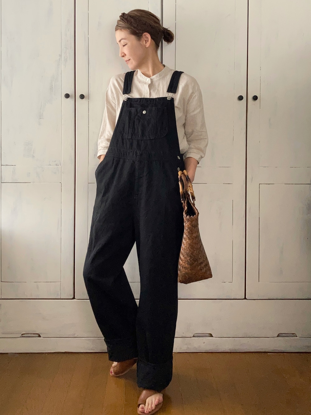 ブラック系のサロペット/オーバーオール、ベージュ系のチュニック、ブラウン系のかごバッグを着用したレディースの春コーディネートの1枚目の写真