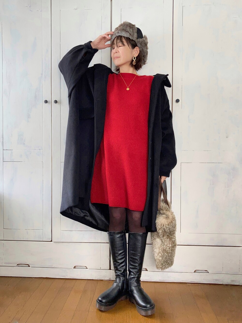 レッド系のワンピース、ブラック系のステンカラーコート、ブラック系のブーツを着用したレディースの冬コーディネートの1枚目の写真