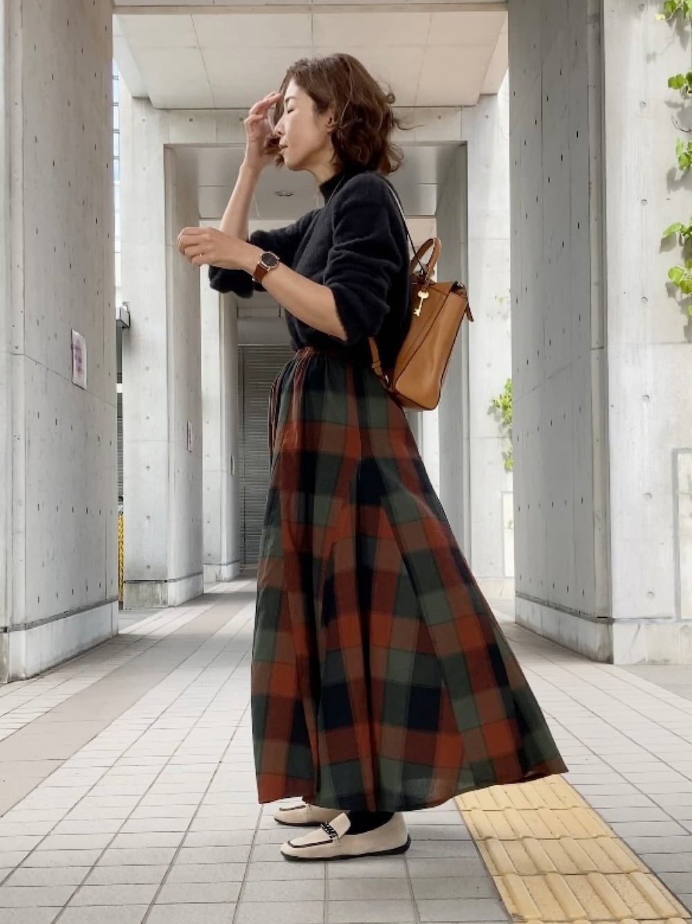 ブラック系のニット/セーター、オレンジ系のスカート、イエロー系のバックパック/リュックを着用したレディースの秋コーディネートの1枚目の写真