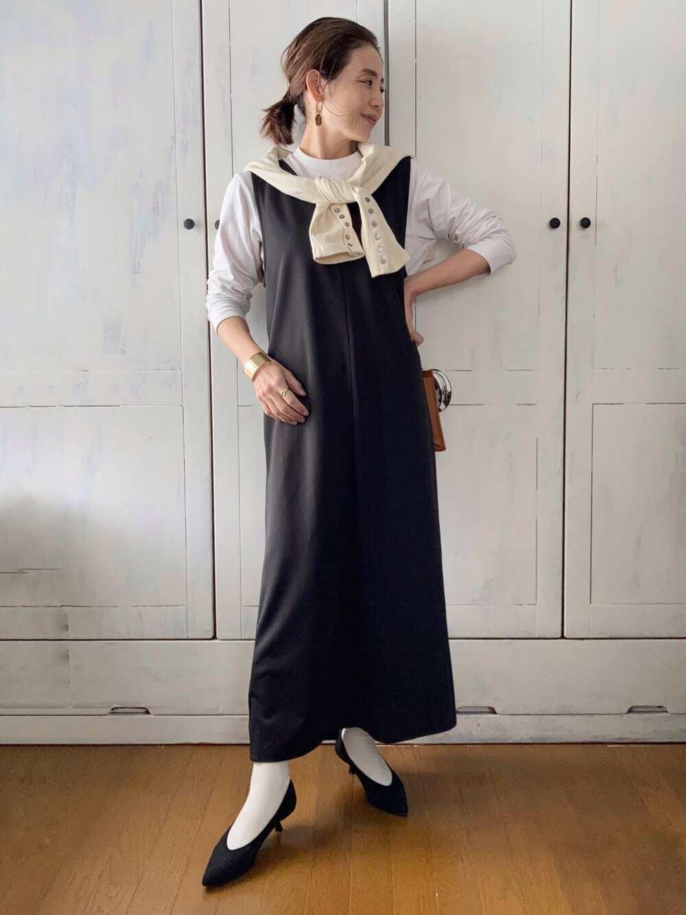 ブラック系のジャンパースカート、ホワイト系のカーディガン/ボレロ、ブラック系のパンプスを着用したレディースの春コーディネートの1枚目の写真