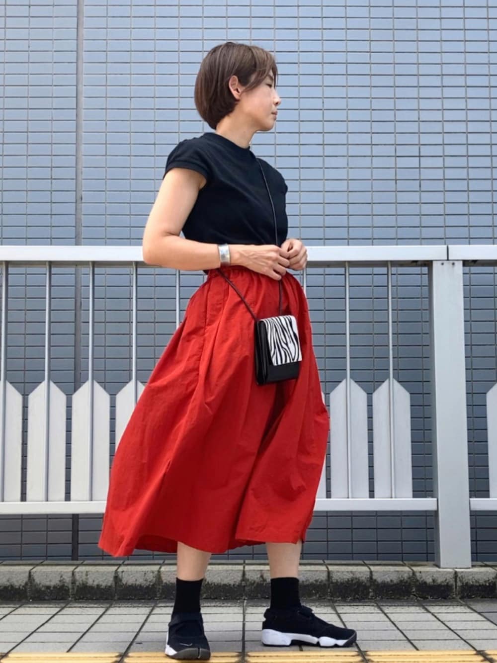 ブラック系のトップス、レッド系のスカート、ブラック系のショルダーバッグを着用したレディースの夏コーディネートの1枚目の写真
