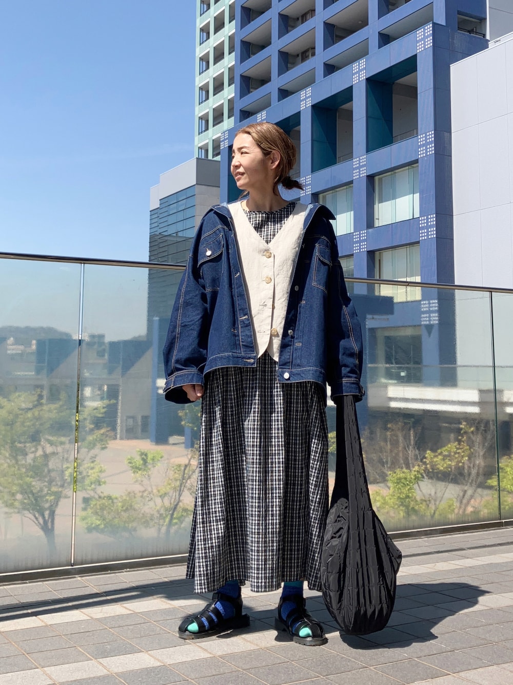 ベージュ系のベスト、ブルー系のデニムジャケット、ブラック系のワンピースを着用したレディースの春コーディネートの1枚目の写真