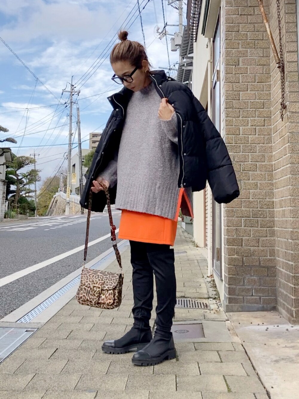 グレー系のニット/セーター、ブラック系のダウンジャケット/コート、オレンジ系のスカートを着用したレディースの冬コーディネートの1枚目の写真