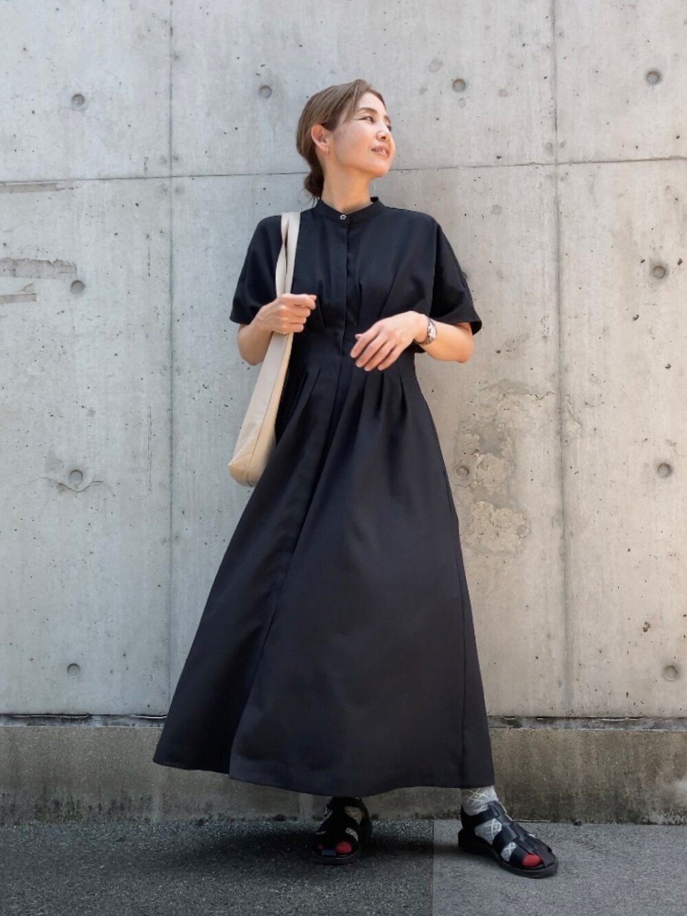 ブラック系のワンピース、ベージュ系のトートバッグ、ブラック系のサンダルを着用したレディースの夏コーディネートの1枚目の写真