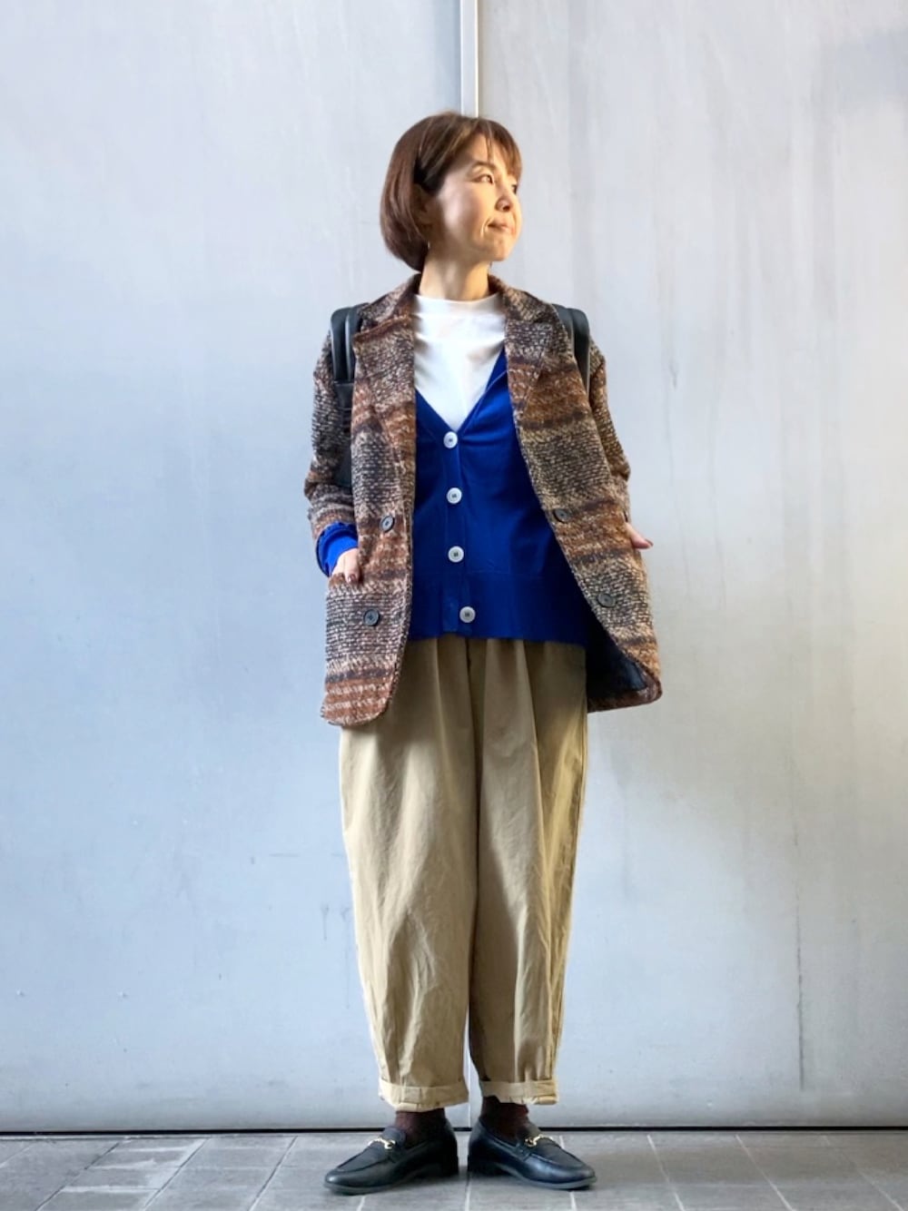 ブラウン系のテーラードジャケット、ブルー系のカーディガン/ボレロ、ブラウン系のバックパック/リュックを着用したレディースの秋コーディネートの1枚目の写真