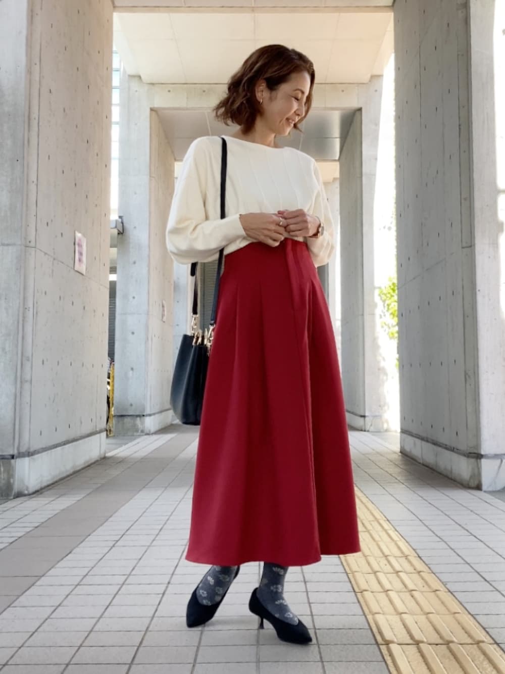 ホワイト系のニット/セーター、レッド系のスカート、ブラック系のハンドバッグを着用したレディースの秋コーディネートの1枚目の写真