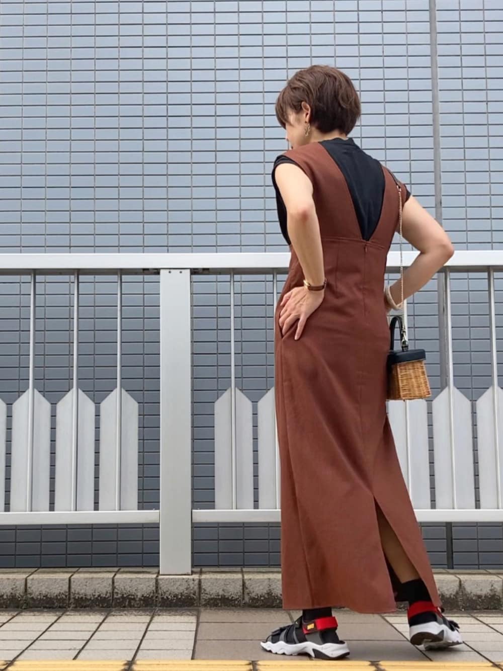 ブラウン系のジャンパースカート、ブラック系のトップス、ブラウン系のかごバッグを着用したレディースの夏コーディネートの1枚目の写真