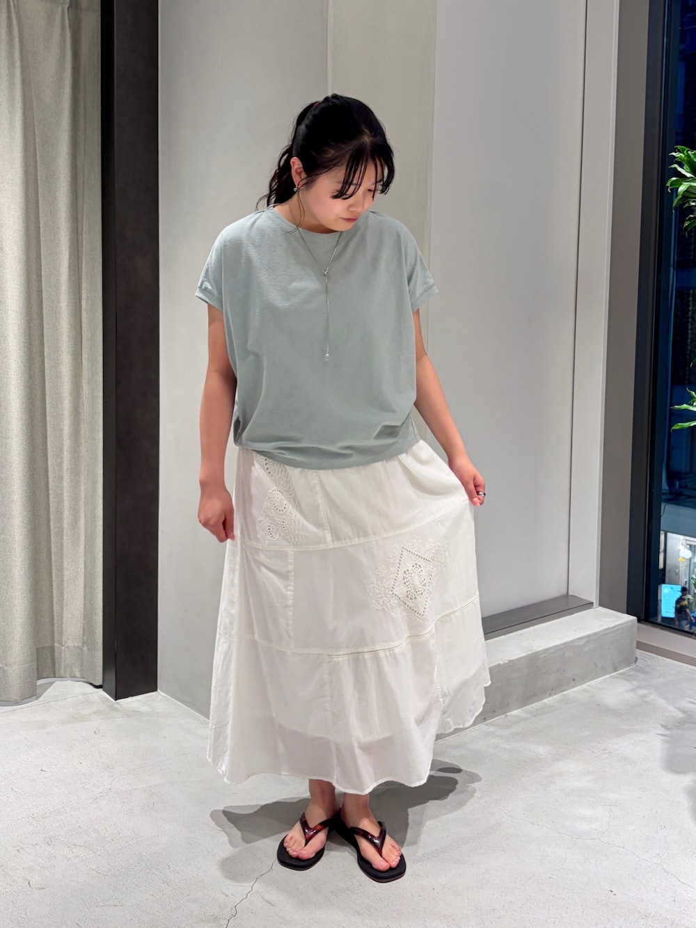 ホワイト系のスカート、ブラック系のサンダル、グリーン系のTシャツ/カットソーを着用したレディースの夏コーディネートの1枚目の写真