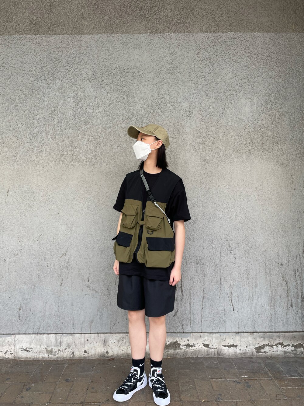 ブラック系のスニーカー、ブラック系のパンツ、グリーン系のベストを着用したレディースの春コーディネートの1枚目の写真