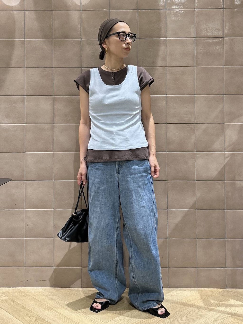 ブラック系のショルダーバッグ、ブラウン系のTシャツ/カットソー、ブルー系のデニムパンツを着用したレディースの夏コーディネートの1枚目の写真
