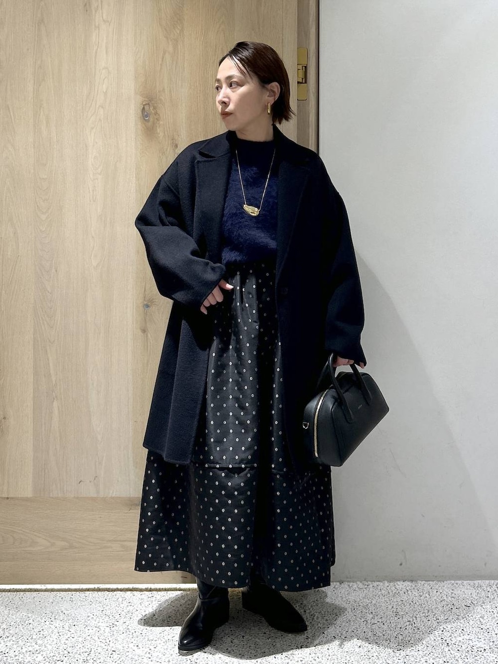 ブルー系のニット/セーター、ブルー系のチェスターコート、ブラック系のスカートを着用したレディースの秋コーディネートの1枚目の写真