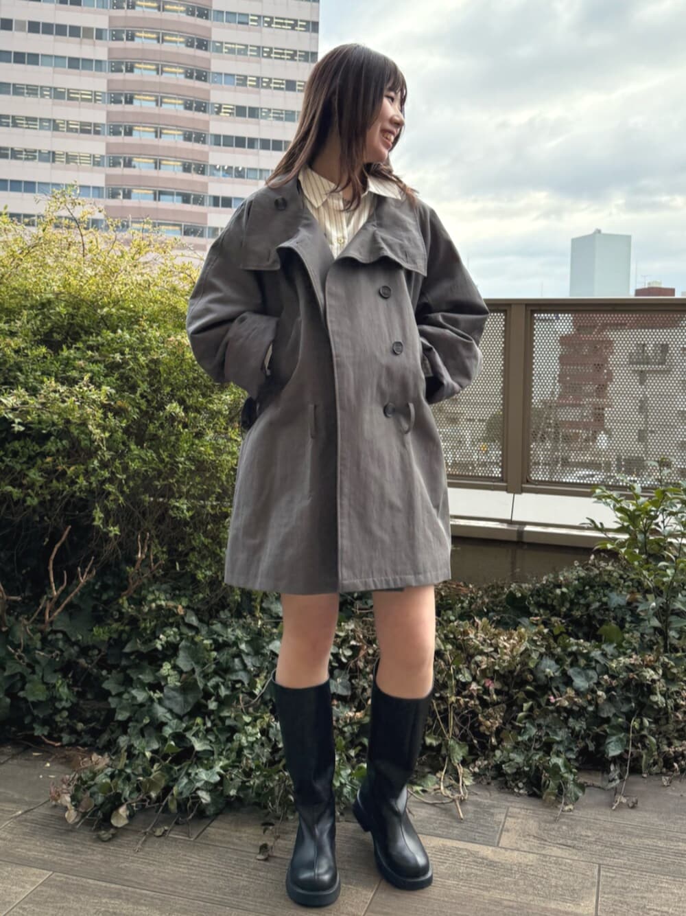 ホワイト系のシャツ/ブラウス、ブラック系のブーツ、グレー系のトレンチコートを着用したレディースの春コーディネートの1枚目の写真