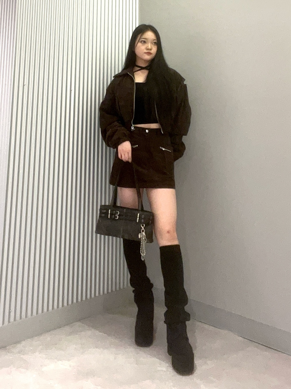 ブラック系のハンドバッグ、ブラック系のブーツ、ブラウン系のスカートを着用したレディースの秋コーディネートの1枚目の写真