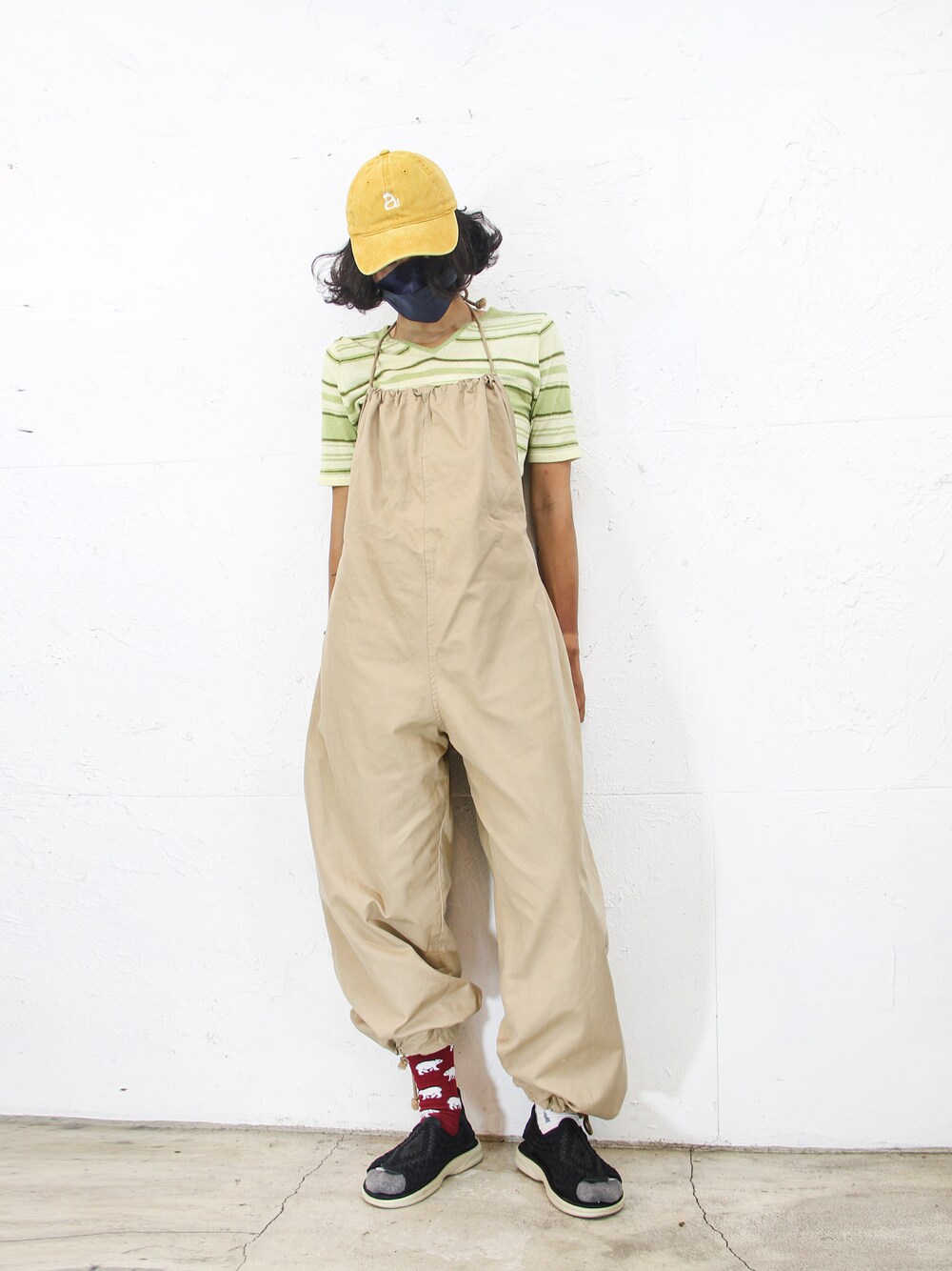 グリーン系のニット/セーター、ベージュ系のサロペット/オーバーオール、イエロー系のキャップを着用したレディースの夏コーディネートの1枚目の写真