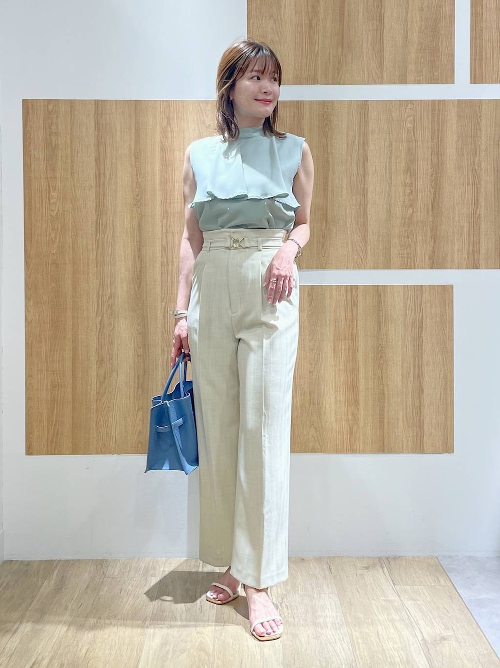 ブルー系のトートバッグ、ベージュ系のスラックス、ホワイト系のサンダルを着用したレディースの夏コーディネートの1枚目の写真