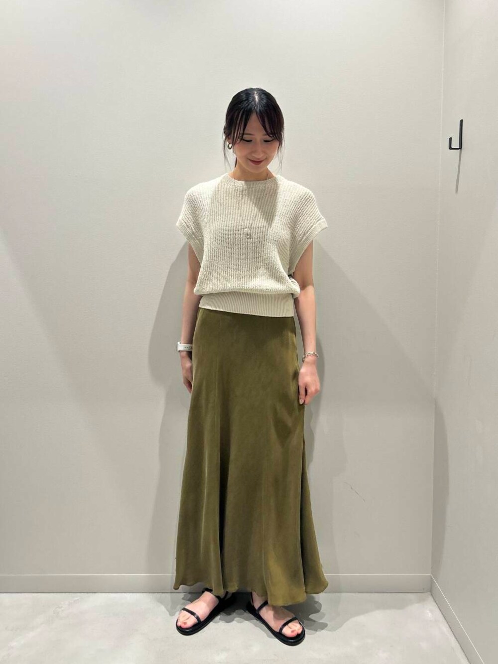 グリーン系のスカート、ブラック系のサンダル、ベージュ系のベストを着用したレディースの夏コーディネートの1枚目の写真