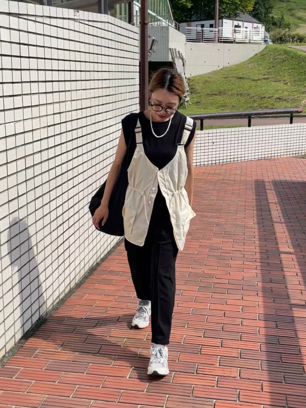 ベージュ系のベスト、ブラック系のその他パンツ、グレー系のスニーカーを着用したレディースの秋コーディネートの1枚目の写真