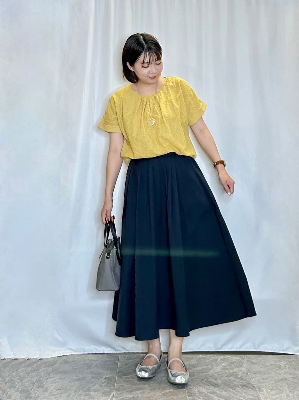 イエロー系のTシャツ/カットソー、ブルー系のスカート、ブラック系のトートバッグを着用したレディースの夏コーディネートの1枚目の写真