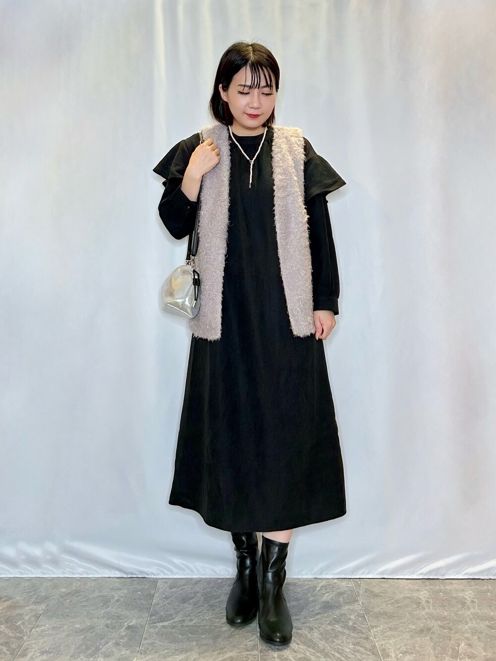 ブラック系のブーツ、シルバー系のショルダーバッグ、グレー系のベストを着用したレディースの秋コーディネートの1枚目の写真