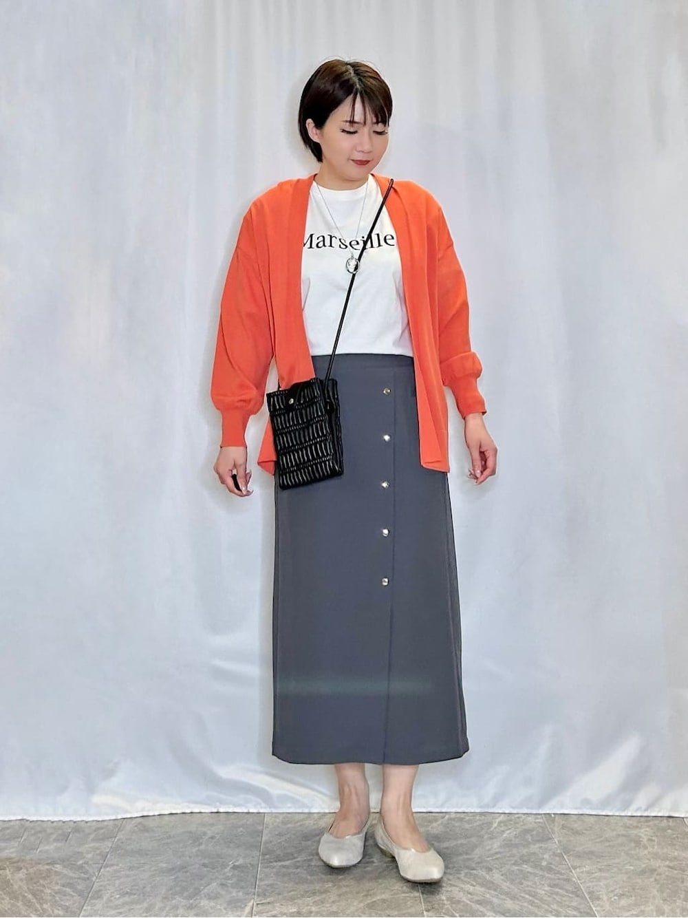 オレンジ系のカーディガン/ボレロ、ホワイト系のTシャツ/カットソー、グレー系のスカートを着用したレディースの春コーディネートの1枚目の写真