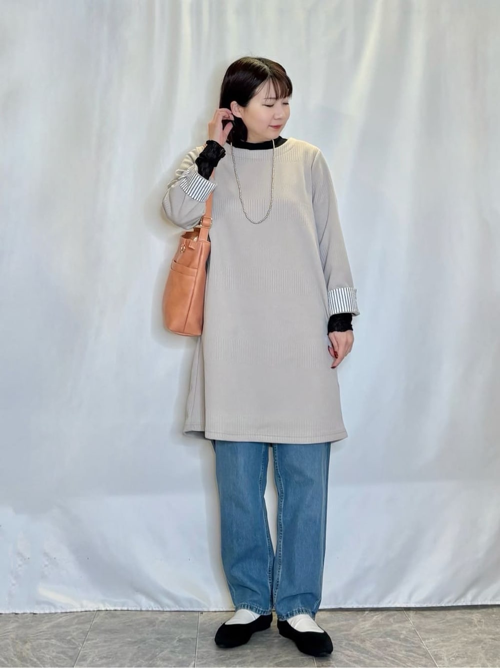 ベージュ系のチュニック、ブラック系のTシャツ/カットソー、ブルー系のデニムパンツを着用したレディースの冬コーディネートの1枚目の写真
