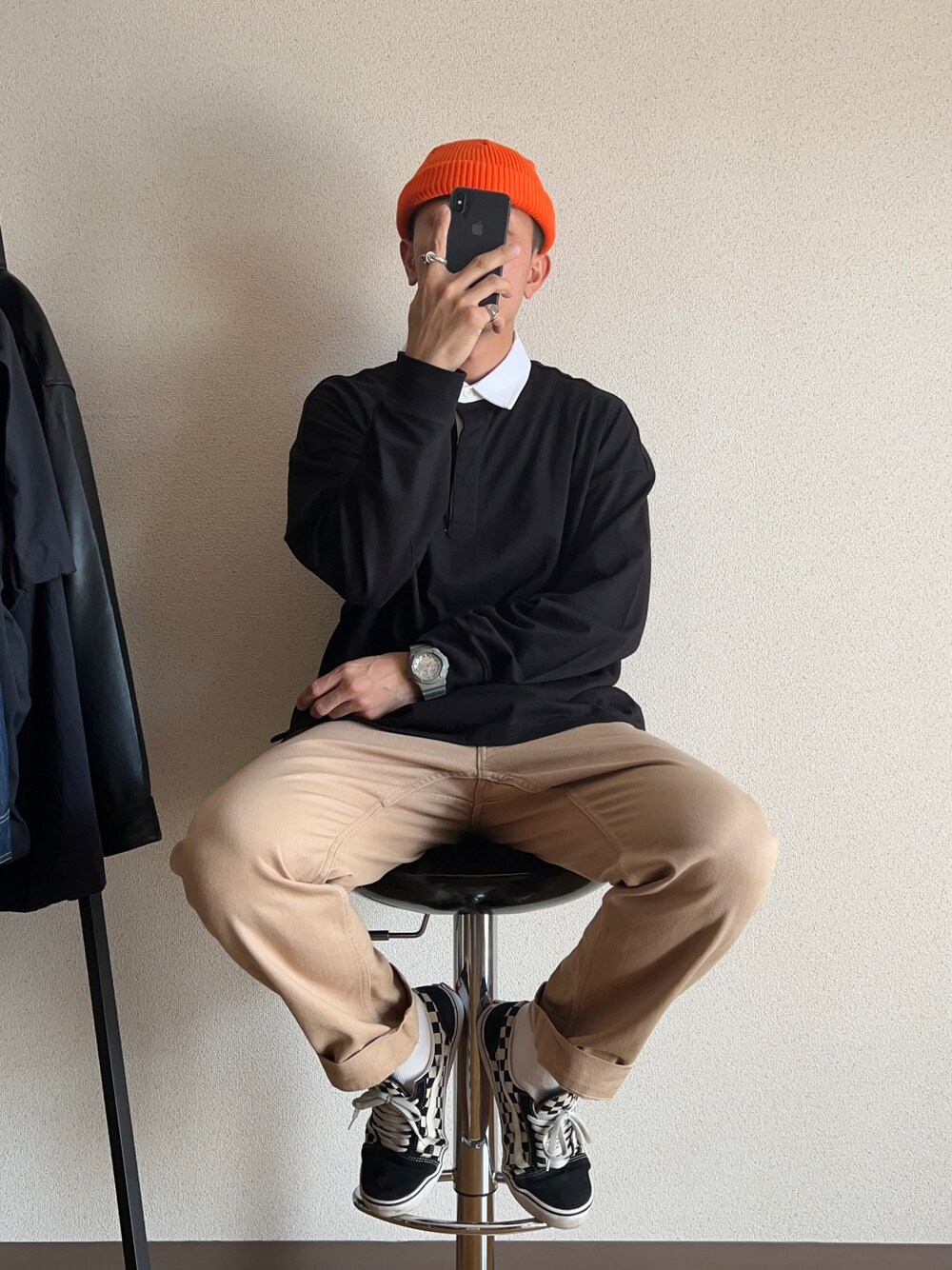 ブラック系のポロシャツ、ベージュ系のチノパンツ、オレンジ系のニットキャップ/ビーニーを着用したメンズの春コーディネートの1枚目の写真