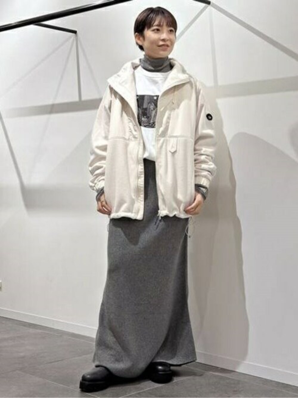 ホワイト系のブルゾン、グレー系のスカート、ブラック系のブーツを着用したレディースの秋コーディネートの1枚目の写真