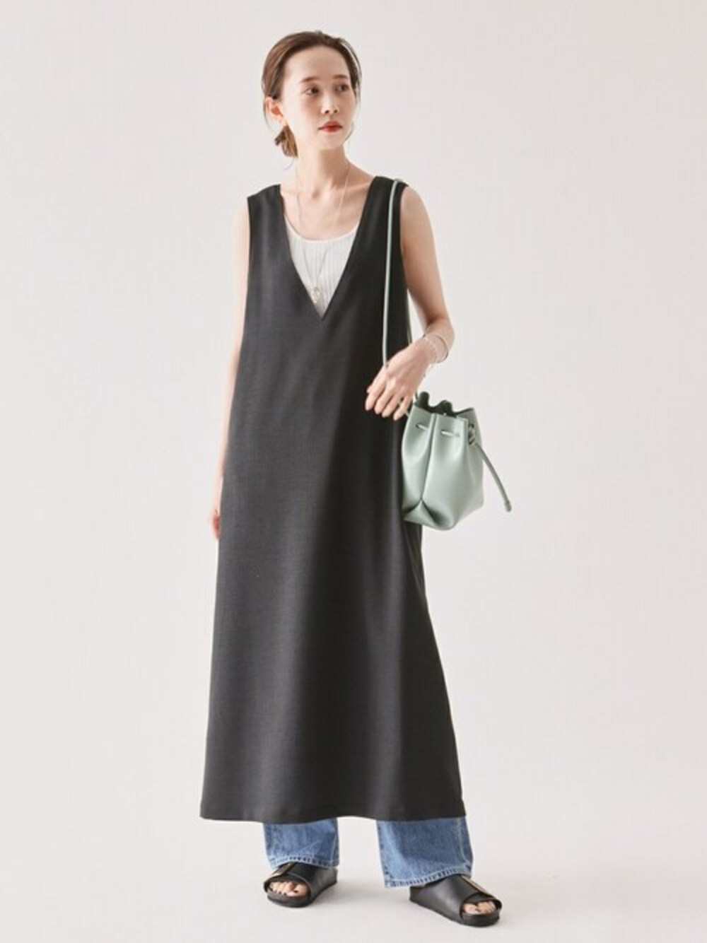 ブラック系のジャンパースカート、グリーン系のショルダーバッグを着用したレディースの春コーディネートの1枚目の写真