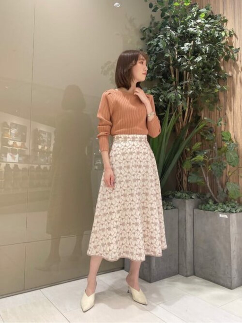 オレンジ系のニット/セーター、ホワイト系のスカートを着用したレディースの春コーディネートの1枚目の写真