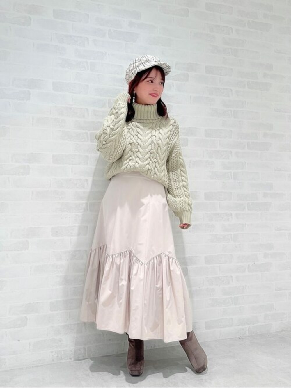 ベージュ系のスカート、グリーン系のニット/セーター、ホワイト系のキャスケットを着用したレディースの秋コーディネートの1枚目の写真