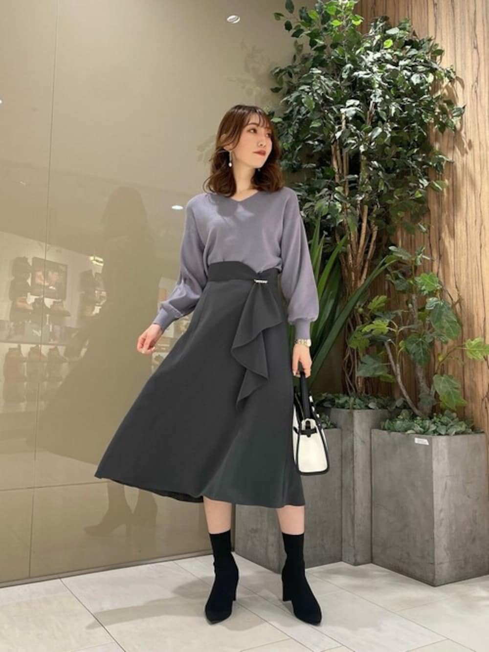 ブルー系のニット/セーター、グレー系のスカート、ホワイト系のショルダーバッグを着用したレディースの冬コーディネートの1枚目の写真