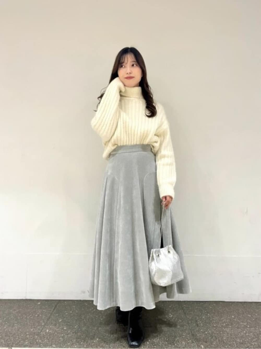 グレー系のスカート、ホワイト系のニット/セーター、シルバー系のショルダーバッグを着用したレディースの冬コーディネートの1枚目の写真