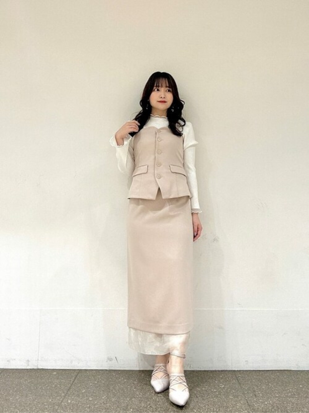 ベージュ系のスカート、ベージュ系のベスト、ホワイト系のニット/セーターを着用したレディースの春コーディネートの1枚目の写真