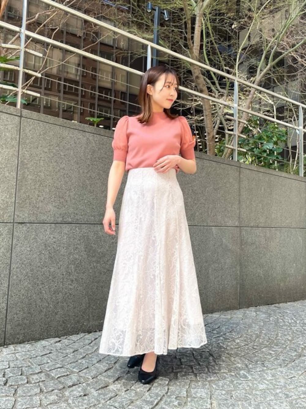 ピンク系のニット/セーター、グレー系のスカート、ブラック系のパンプスを着用したレディースの春コーディネートの1枚目の写真