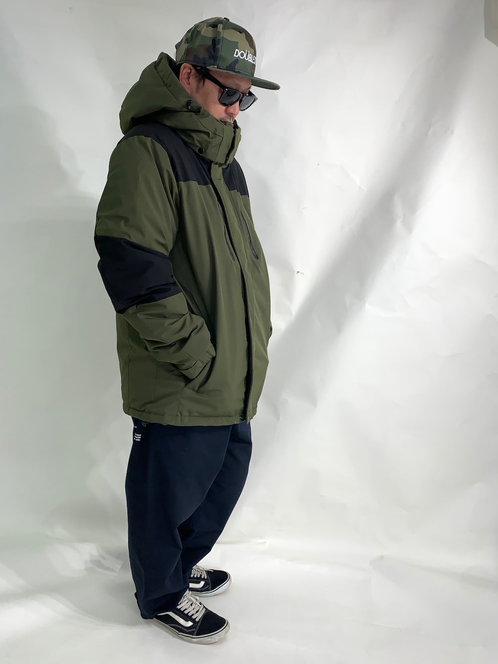 ブラック系のスニーカー、ブルー系のデニムパンツ、グリーン系のナイロンジャケットを着用したメンズの冬コーディネートの1枚目の写真