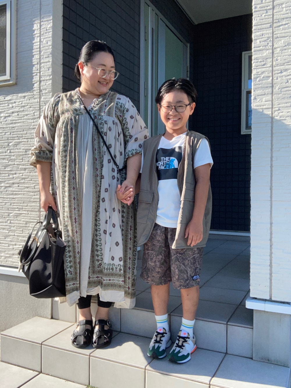 ベージュ系のワンピース、ブラック系のサンダル、ブラック系のハンドバッグを着用したレディースの夏コーディネートの1枚目の写真