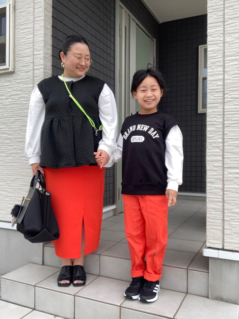 ブラック系のベスト、ブルー系のTシャツ/カットソー、オレンジ系のスカートを着用したレディースの春コーディネートの1枚目の写真