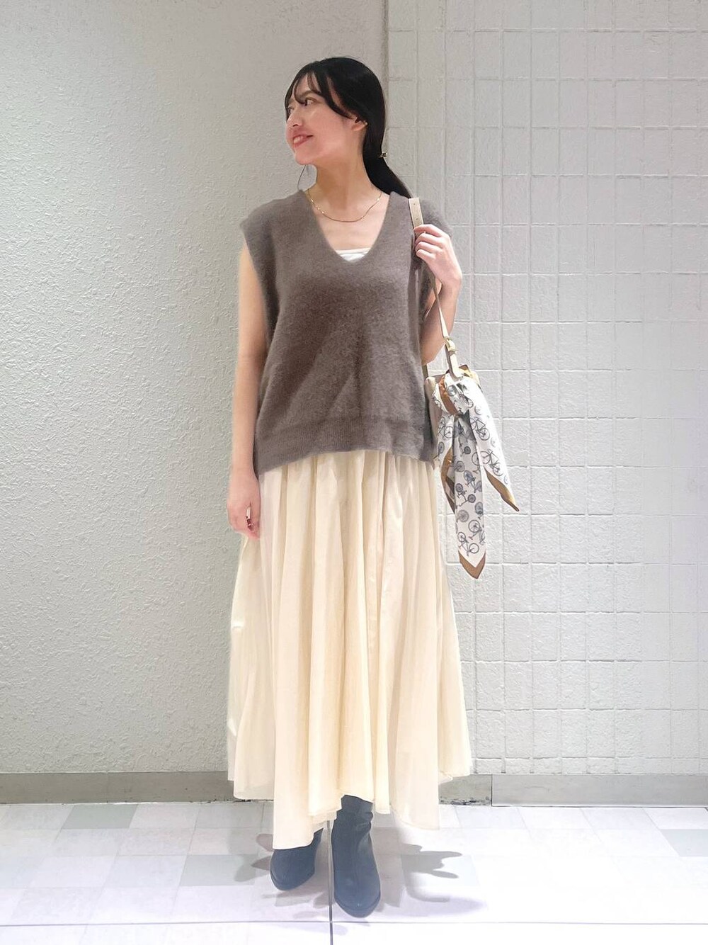 ブラック系のブーツ、ブラウン系のベスト、ホワイト系のスカートを着用したレディースの秋コーディネートの1枚目の写真