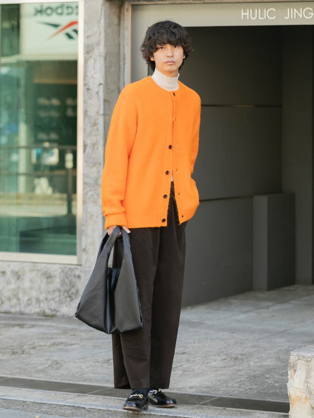 オレンジ系のカーディガン/ボレロ、ホワイト系のニット/セーター、ブラック系のローファーを着用したメンズの秋コーディネートの1枚目の写真