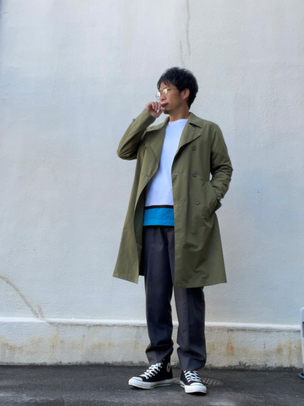 グリーン系のトレンチコート、ホワイト系のTシャツ/カットソー、グレー系のスラックスを着用したメンズの秋コーディネートの1枚目の写真