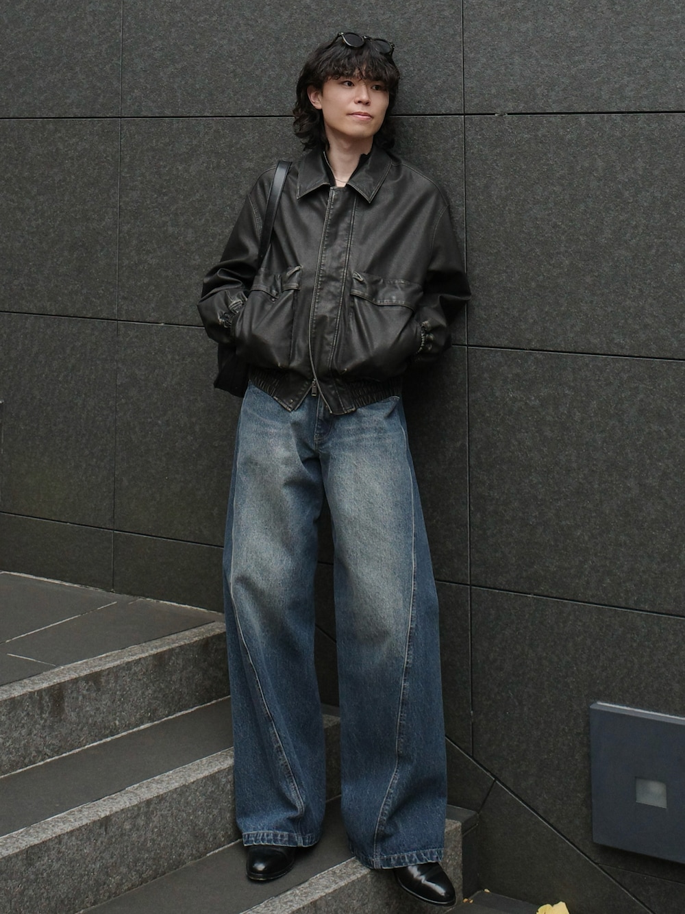 グレー系のブルゾン、ブラック系のショルダーバッグ、ブルー系のデニムパンツを着用したメンズの秋コーディネートの1枚目の写真