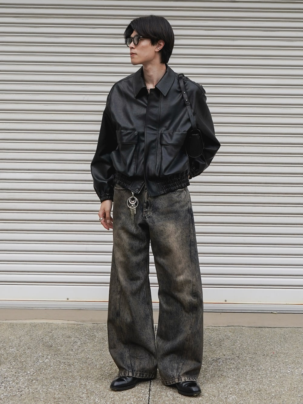 ブラック系のブルゾン、ブラック系のショルダーバッグ、ブルー系のデニムパンツを着用したメンズの秋コーディネートの1枚目の写真