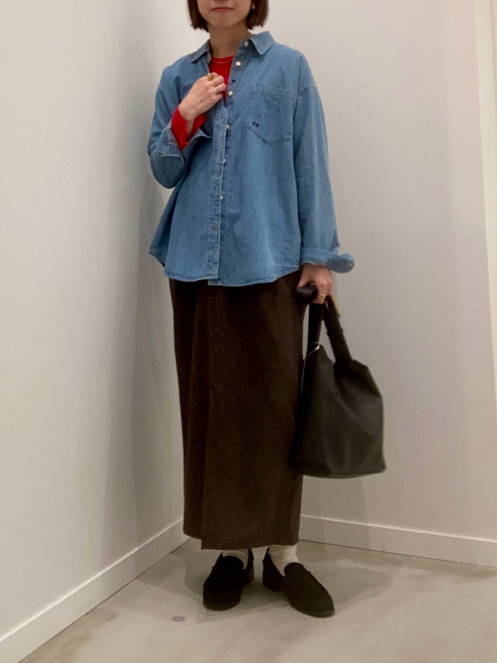 レッド系のニット/セーター、ブルー系のシャツ/ブラウス、ブラウン系のスカートを着用したレディースの冬コーディネートの1枚目の写真