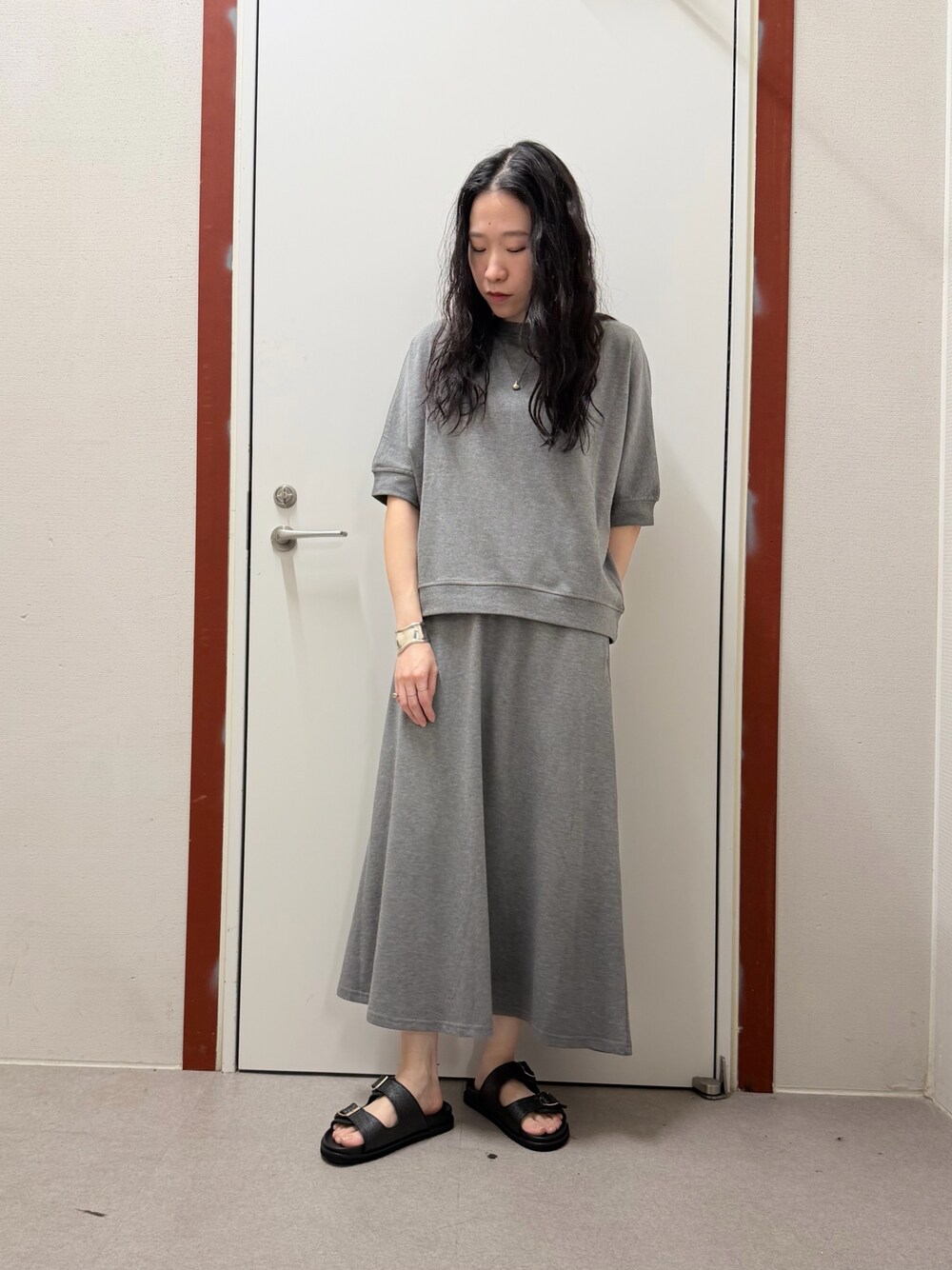 グレー系のTシャツ/カットソー、ホワイト系のスカート、ブラック系のサンダルを着用したレディースの春コーディネートの1枚目の写真