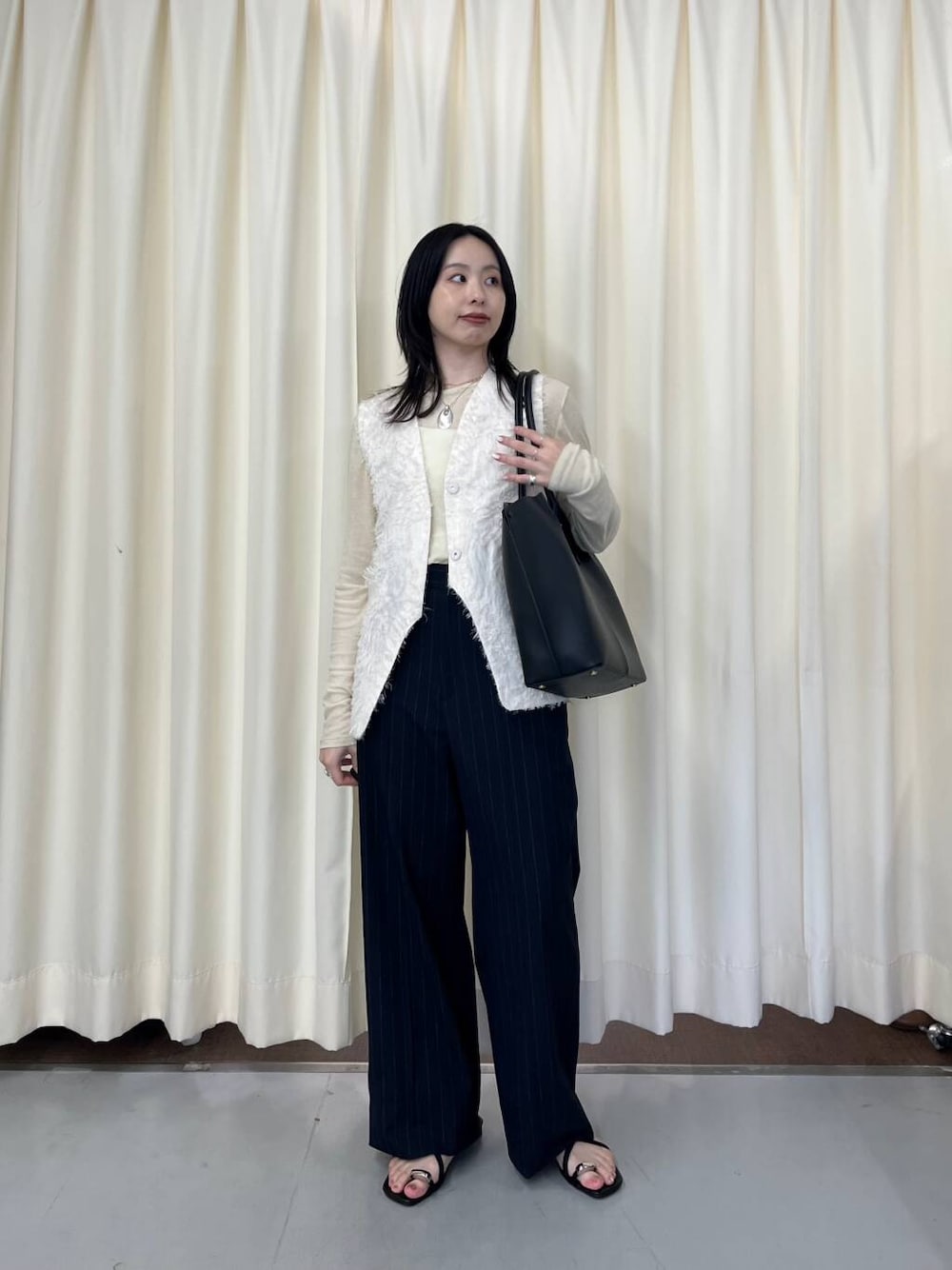 ホワイト系のベスト、ブラック系のサンダル、ブラック系のショルダーバッグを着用したレディースの春コーディネートの1枚目の写真