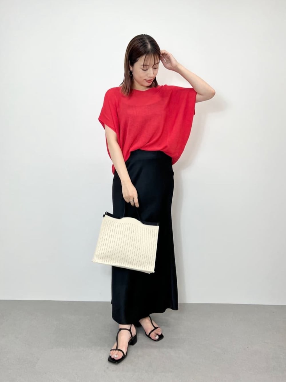 ピンク系のニット/セーター、ブラック系のスカート、ホワイト系のハンドバッグを着用したレディースの夏コーディネートの1枚目の写真