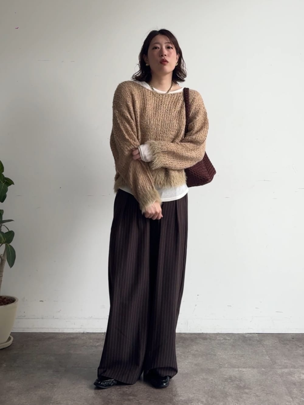 イエロー系のニット/セーター、ブラウン系のスラックス、ホワイト系のTシャツ/カットソーを着用したレディースの秋コーディネートの1枚目の写真