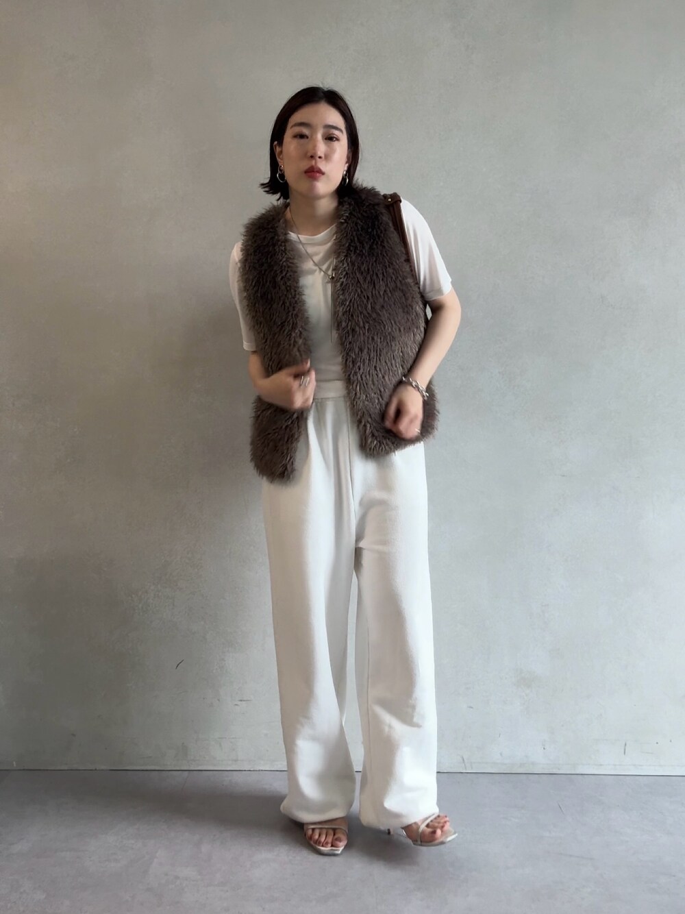 ホワイト系のスウェットパンツ、グレー系のベスト、ブラウン系のショルダーバッグを着用したレディースの秋コーディネートの1枚目の写真